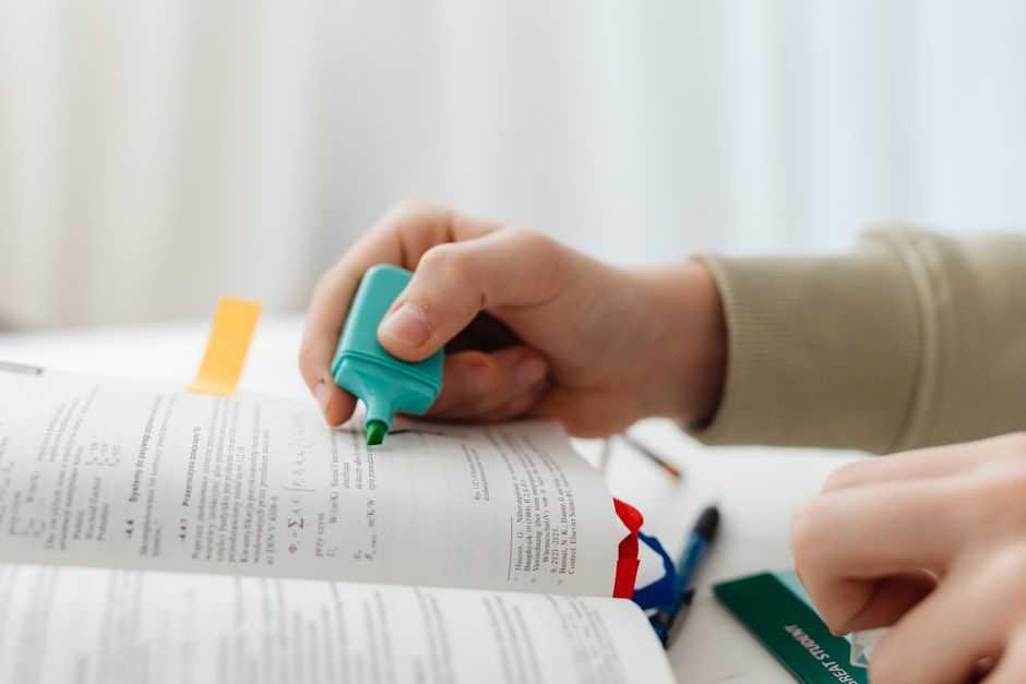 Hand highlighting text in a book using a green marker, capturing a focused study moment.